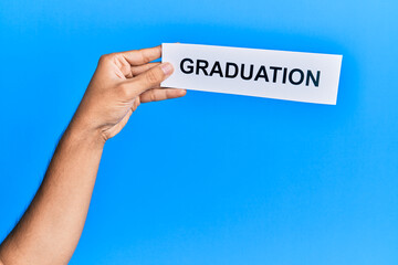 Hand of caucasian man holding paper with graduation word over isolated blue background