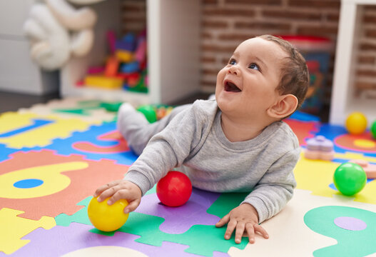 Adorable hispanic baby playing with balls lying on floor at kindergarten