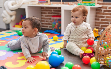 Two adorable babies playing with balls sitting on floor at kindergarten