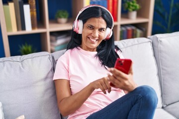Middle age hispanic woman listening to music sitting on sofa at home