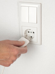 Strom und Energieverbrauch. Hand beim Einstecken eines weißen Steckers in die weiße Steckdose an der Wand