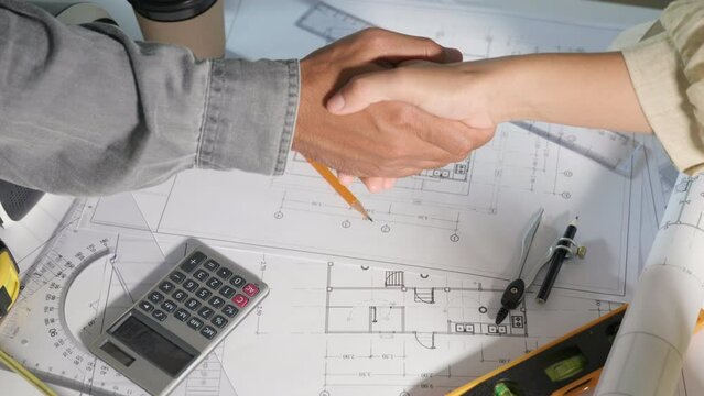 Architect team success and handshaking after meeting consult and work for architectural construction project with partner editing on blueprint paper plans, Architect and engineer shaking hands