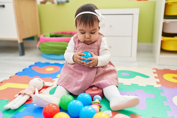 Fototapeta na wymiar Adorable hispanic baby playing with balls sitting on floor at kindergarten