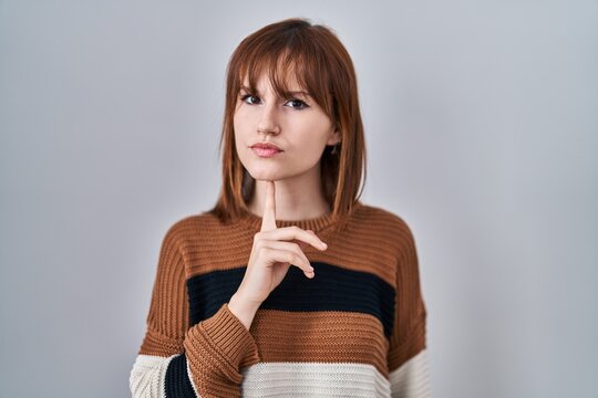 Young beautiful woman wearing striped sweater over isolated background thinking concentrated about doubt with finger on chin and looking up wondering