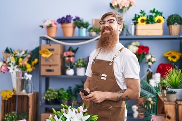 Young redhead man florist smiling confident using smartphone at flower shop - obrazy, fototapety, plakaty