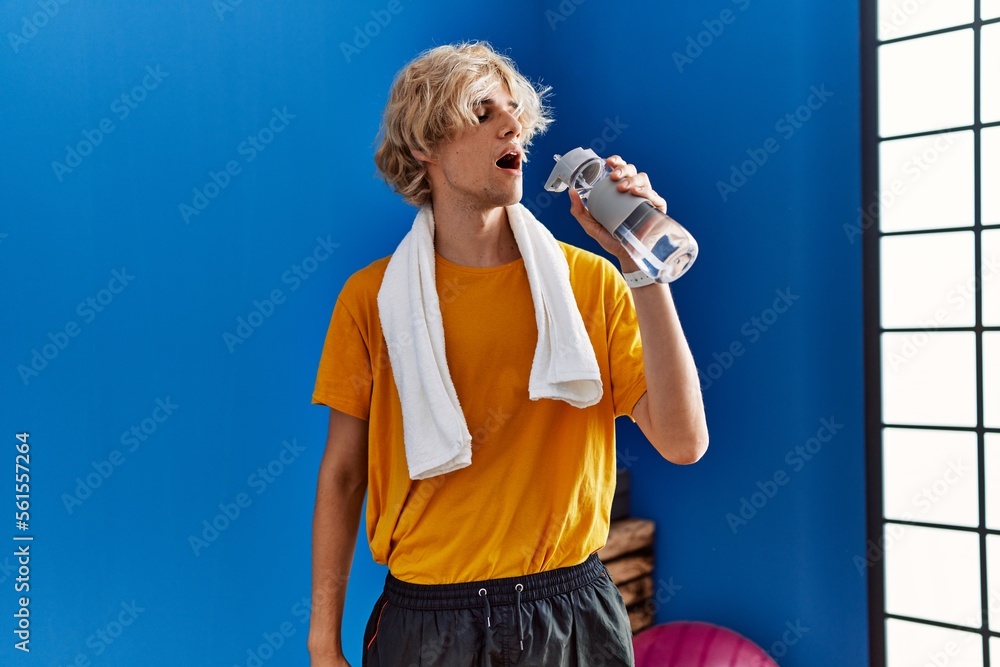 Sticker young blond man smiling confident drinking water at sport center