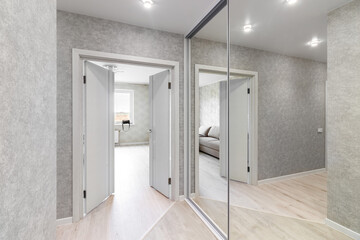 Part of the corridor of a residential building. At the end of the room there is a door, on the right is a wardrobe with a mirror that can be seen, reflecting the view of the room