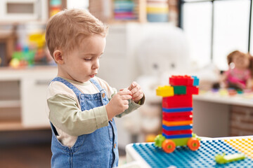 Adorable toddler playing with construction blocks standing at kindergarten