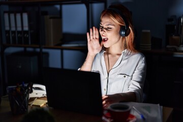 Young caucasian woman working at the office at night shouting and screaming loud to side with hand on mouth. communication concept.