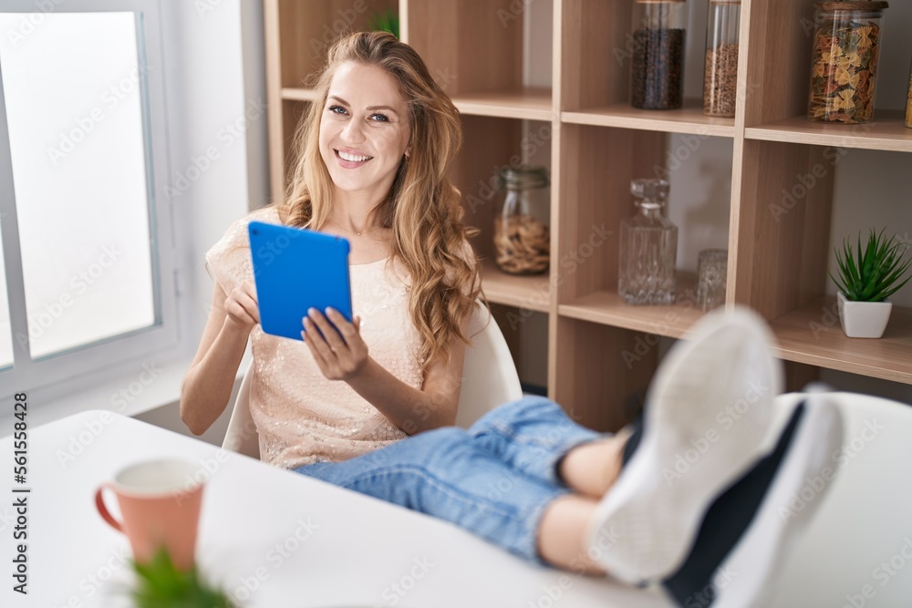 Poster Young blonde woman using touchpad drinking coffee at home