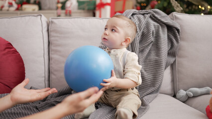 Adorable toddler sitting on sofa by christmas tree with playing with ball at home