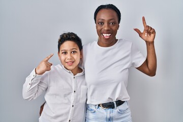 Fototapeta premium Young mother and son standing together over white background smiling amazed and surprised and pointing up with fingers and raised arms.