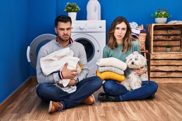 Young hispanic couple doing laundry sitting on the floor skeptic and nervous, frowning upset because of problem. negative person.
