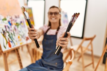 Young woman smiling confident holding paintbrushes at art studio