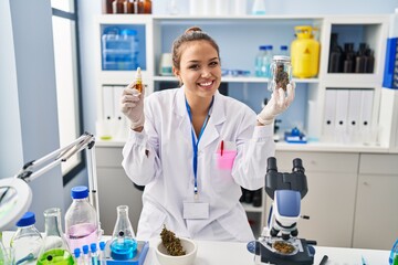 Young hispanic woman doing weed oil extraction at laboratory smiling with a happy and cool smile on face. showing teeth.