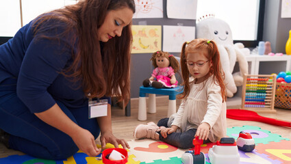 Teacher and student playing supermarket game sitting on floor at kindergarten