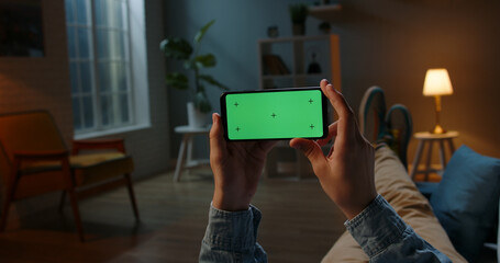 Close up shot of guy using his horizontal smart phone with mock up green screen at night, using...
