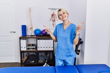 Young physiotherapist woman working at pain recovery clinic smiling confident pointing with fingers to different directions. copy space for advertisement