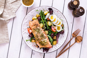 A top down view of a salmon Nicoise salad on a rustic table, ready for eating.