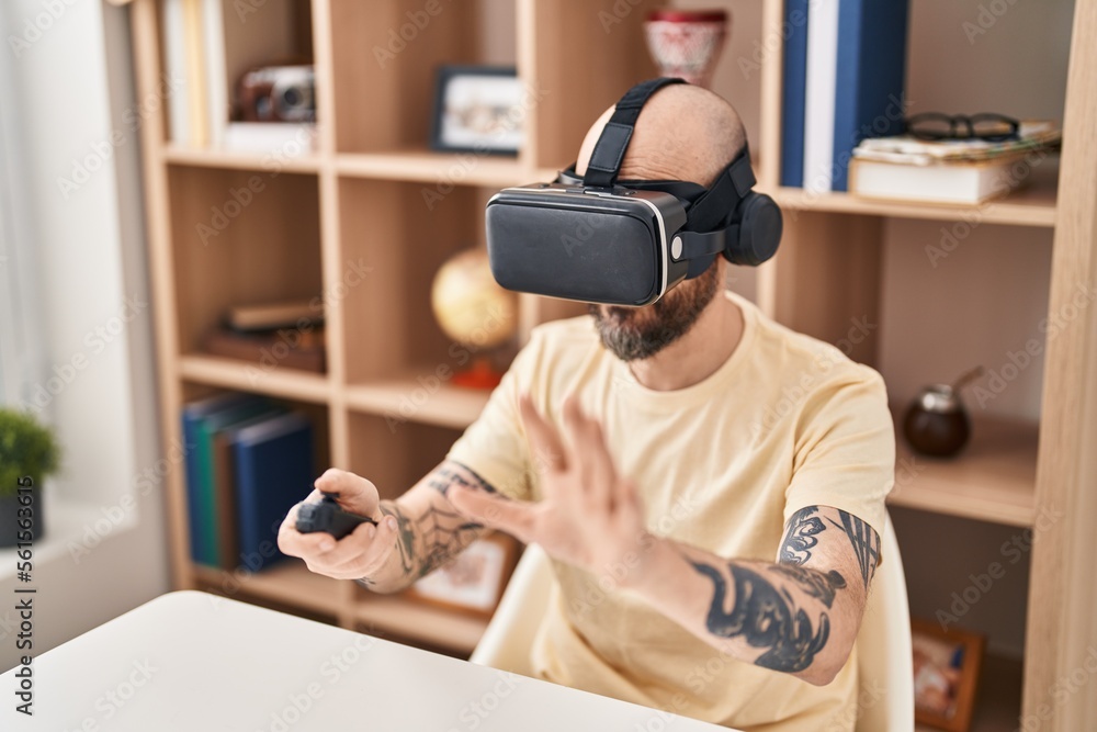 Sticker Young bald man playing video game using virtual reality glasses at home