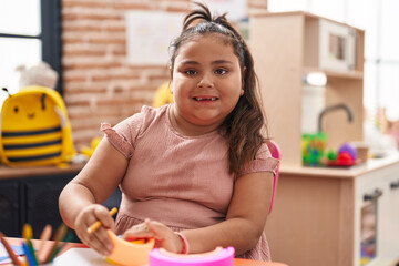 Plus size hispanic girl playing with toy sitting on table at kindergarten