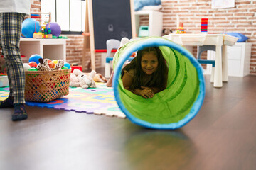 Plus size hispanic girl smiling confident crawling through tunnel toy at classroom