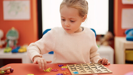 Adorable blonde girl playing with maths puzzle game sitting on table at kindergarten