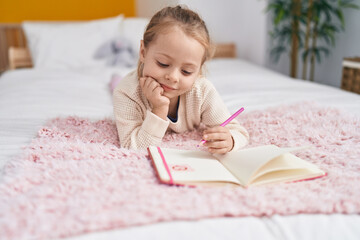 Adorable blonde girl drawing on notebook lying on bed at bedroom