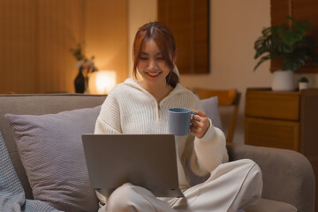 Winter season concept, Young woman drinks tea and watching movie on laptop at night time in winter