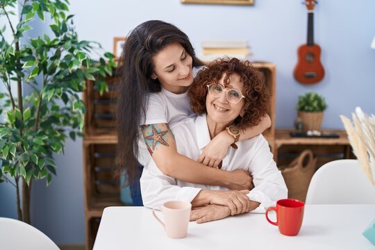 Two women mother and daughter drinking coffee hugging each other at home