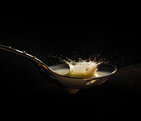 golden spoon and splashing milk on black background. Pouring milk