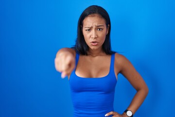 Fototapeta na wymiar Hispanic woman standing over blue background pointing displeased and frustrated to the camera, angry and furious with you