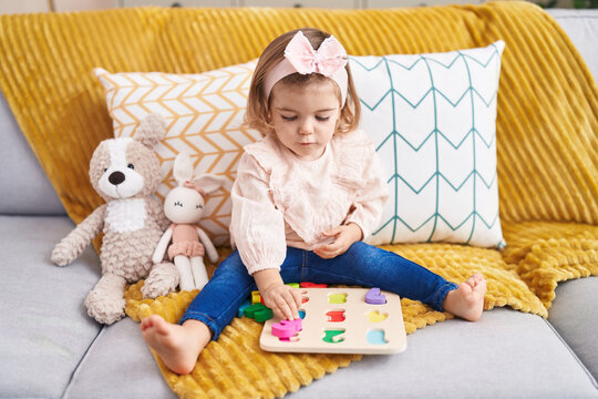 Adorable blonde toddler playing with maths puzzle game sitting on sofa at home