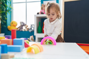 Adorable blonde girl playing with toys standing at kindergarten