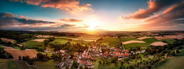 Aerial panorama of a village surrounded by fields at sunrise, with beautiful colorful sky and warm...