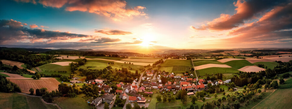 Aerial panorama of a village surrounded by fields at sunrise, with beautiful colorful sky and warm light