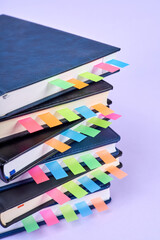 Close-up of a stack of office notepads with colorful sticky page markers sandwiched between pages on purple background