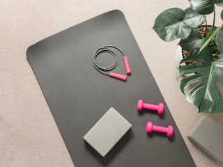 Stylish gray and pink home fitness flat lay. Top view of gray sport mat, yoga block, skipping rope...