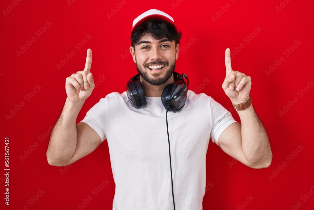 Canvas Prints Hispanic man with beard wearing gamer hat and headphones smiling amazed and surprised and pointing up with fingers and raised arms.