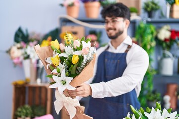 Young hispanic man florist holding bouquet of flowers at florist shop