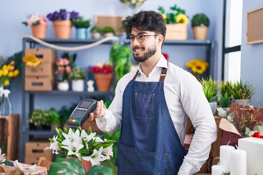 Young hispanic man florist smiling confident holding dataphone at florist shop