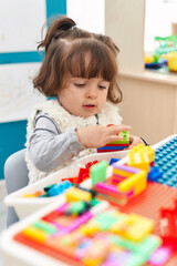 Adorable hispanic toddler playing with construction blocks sitting on table at kindergarten