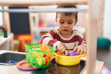 Adorable toddler playing with play kitchen standing at kindergarten