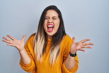 Young hispanic woman standing over isolated background celebrating mad and crazy for success with...