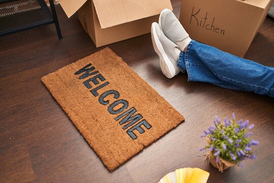 Young blonde woman sittng on the floor near of welcome doormat at new home