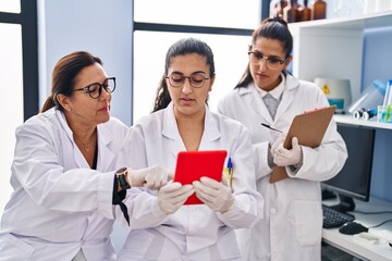 Fototapeta premium Three woman scientists using touchpad write on checklist at laboratory