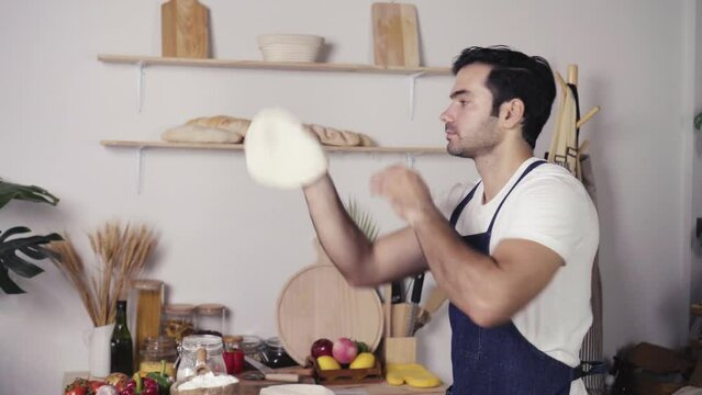 Handsome Cacuasian Man Tossing Pizza Dough In The Air In Small Business Pizza Homemade.