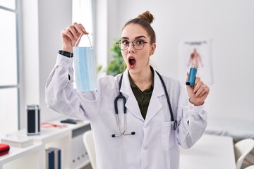 Young hispanic girl holding medical asthma inhaler at the clinic afraid and shocked with surprise and amazed expression, fear and excited face.