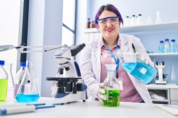 Young beautiful plus size woman scientist pouring liquid on test tube at laboratory