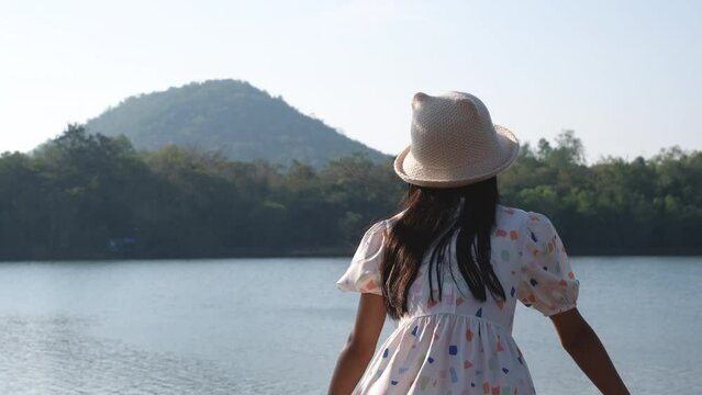 Asian girl wearing a hat stands with her back looking at the scenery by the lake.